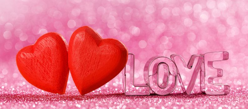 Two red handmade wooden hearts and word love on pink bright glitter lights bokeh background