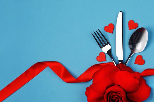 Cutlery set tied with silk ribbon rose flower and hearts on blue background Valentine day dinner concept