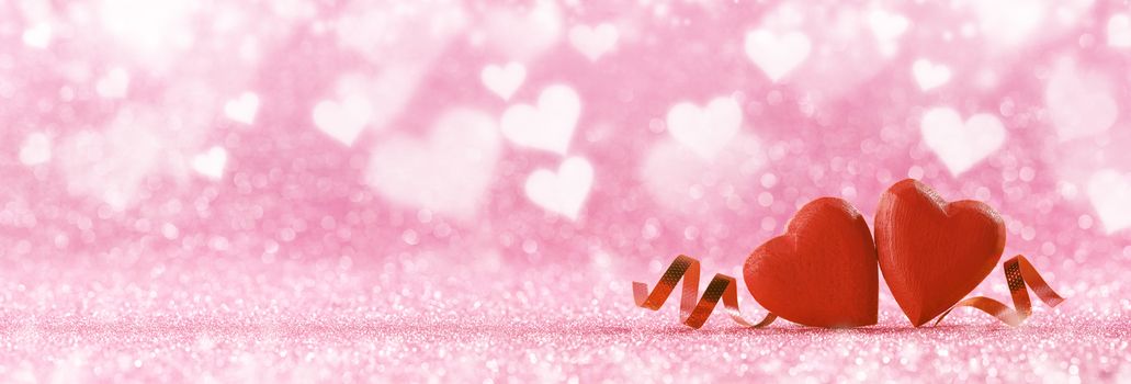 Two red handmade wooden hearts and ribbons on pink bright glitter lights bokeh background