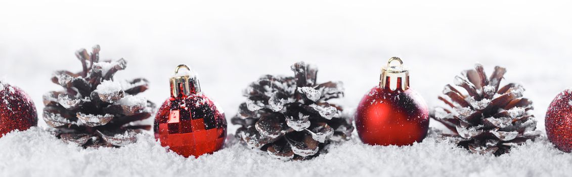 Red Christmas balls and pine cones in a row in snow isolated on white background