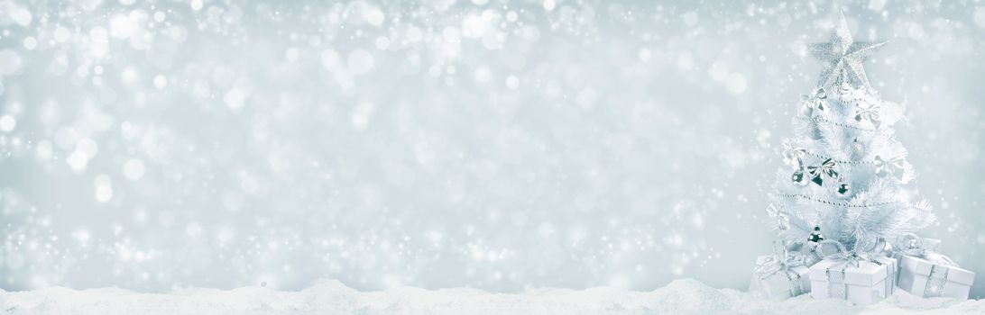 White christmas tree with silver decorations and gifts on snow on bokeh background