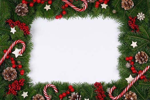 Christmas Border frame of tree branches on white background with copy space isolated, red and white decor, berries, stars, cones