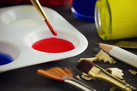 Closeup artist paint brush above color plate and poster color bottle on table. Concept of art education.