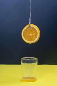 a slice of orange hanging by a thread over a glass