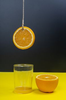 a slice of orange hanging by a thread over a glass