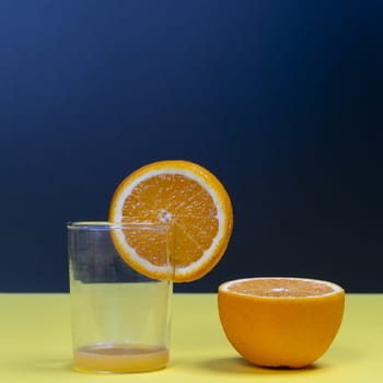 An orange fruit sliced and a glass on a yellow surface
