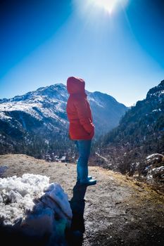 A woman in winter warm clothing standing on top of the rock of a snowcapped rocky mountain peak. Rear view. Deep Snow and Blizzard all around. Human face to face with beauty in nature concept.