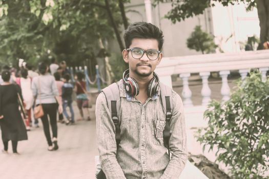 Half length portrait of attractive young a man called Ahok standing outside school building with modern headphone and looking at camera. A music student portrait photography on 21 June World Music Day