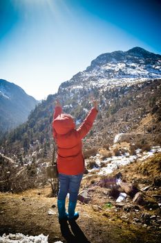 A woman in winter clothing standing on top of the rock of a snowcapped rocky mountain. Rear view. Deep Snow and Blizzard all around. Human face to face with beauty in nature concept.