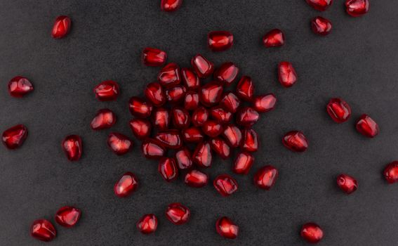 Pomegranate seeds on black background, top view