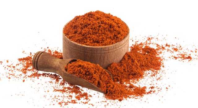 Pile of red paprika powder in wooden bowl and scoop isolated on white background