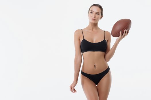 Attractive erotic young woman in lingerie holding rugby ball and looking at camera