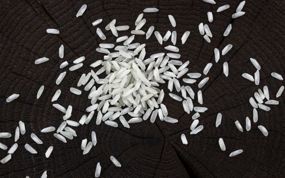 Heap of rice groats on black wooden background, top view