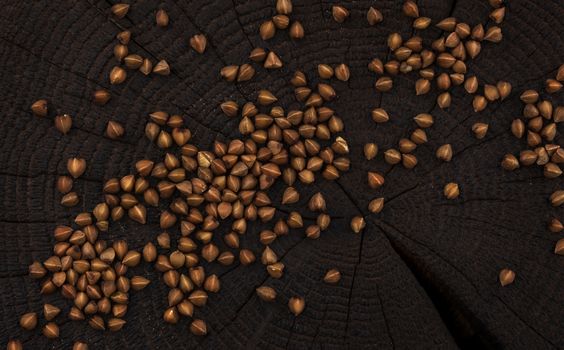 Heap of buckwheat grain on black wooden background, top view