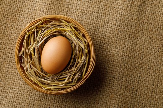 Chicken or hen egg on straw in wicker basket on sackcloth background