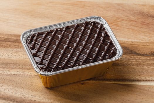 Chocolate cake in aluminium foil tray on wooden table or cutting board, deep focus stacking image