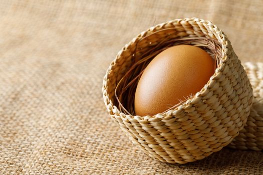 Chicken or hen egg in wicker basket on sackcloth background