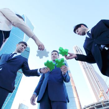 Business people assembling jigsaw puzzle near skyscrapers