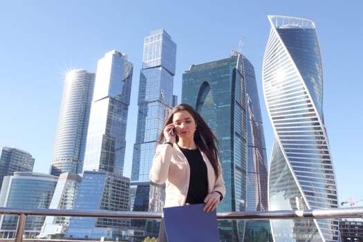 Young beautiful businesswoman with cellphone outdoors at skyscraper background