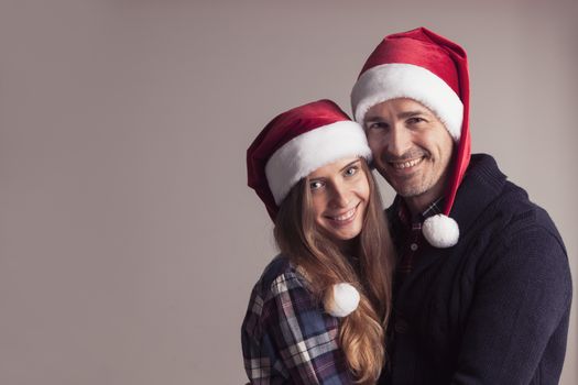 Happy smiling couple in Santa hats on gray background