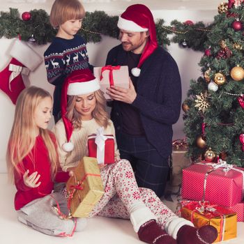 Cheerful family with Christmas gifts sitting near decorated Christmas tree