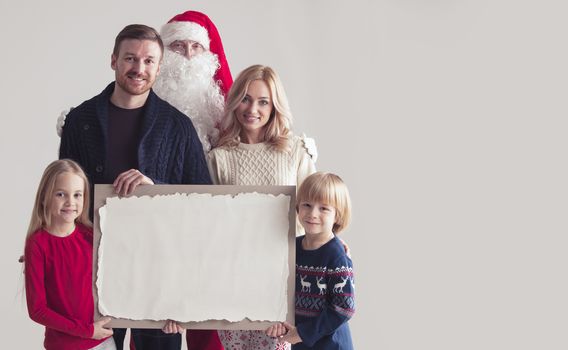 Christmas portrait of happy smiling family with two children and Santa Claus embracing them holding blank vintage paper