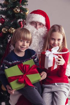 Portrait of smiling little children sitting on santa claus knees near christmas tree