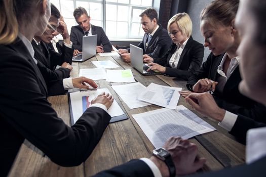 Group of diverse business executives holding a meeting around a table discussing graphs charts showing statistical data analysis