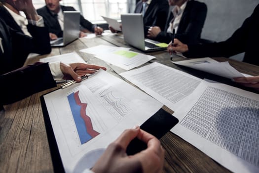Group of diverse business executives holding a meeting around a table discussing graphs charts showing statistical data analysis