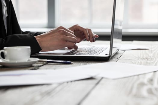 Young businessman in black suit using laptop in office