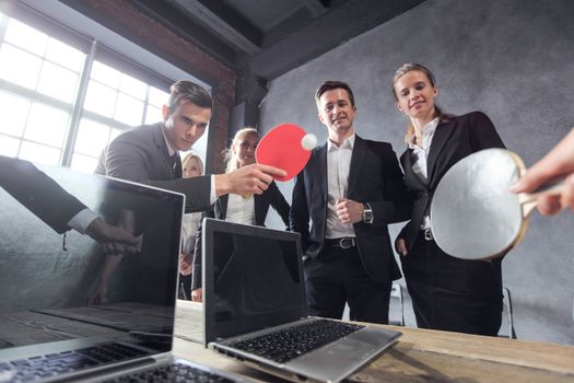 Business people play ping pong on office table with laptops