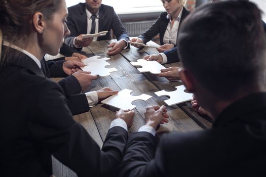 Business people and puzzle on wooden table, teamwork concept