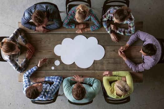 Hipster business teamwork brainstorming planning meeting concept, people sitting around the table with white paper shaped like dialog cloud