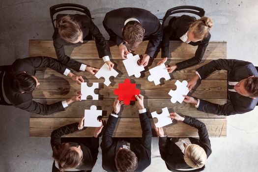 Business people and puzzle on wooden table, teamwork concept