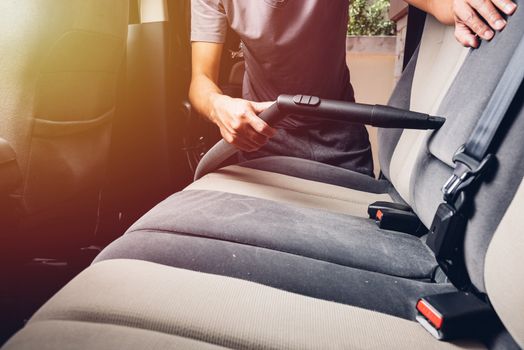 Worker man cleaning dust interior vacuum inside car