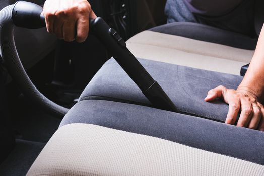 Worker man cleaning dust interior vacuum inside car after wash