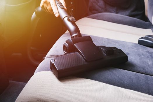 Worker man cleaning dust interior vacuum inside car after wash