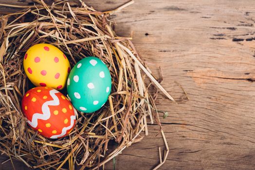 Beautiful Easter multi color egg in straw on wooden background, Easter day concept