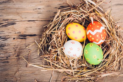 Beautiful Easter multi color egg in straw on wooden background, Easter day concept