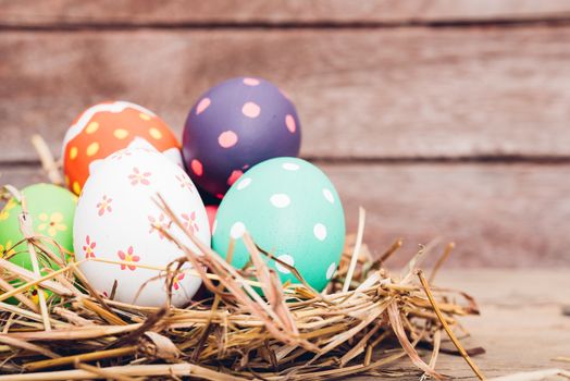 Beautiful Easter multi color egg in straw on wooden background, Easter day concept