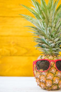 Holiday pineapple have sunglasses on yellow wooden background, tropical holiday concept