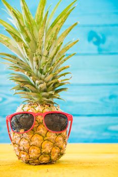 Holiday pineapple have sunglasses on blue wooden background, tropical holiday concept