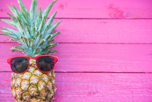 Holiday pineapple have sunglasses on pink    wooden background, tropical holiday concept