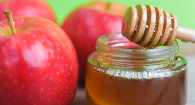 Jewish holiday, Apples Rosh Hashanah on the photo have honey in jar and red apples on wooden with green background