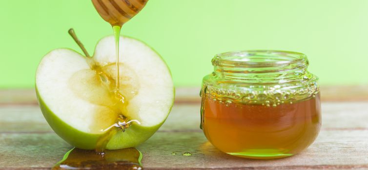 Jewish holiday, Apple Rosh Hashanah, on the photo have honey in jar and drop honey on green apples on wooden with green background