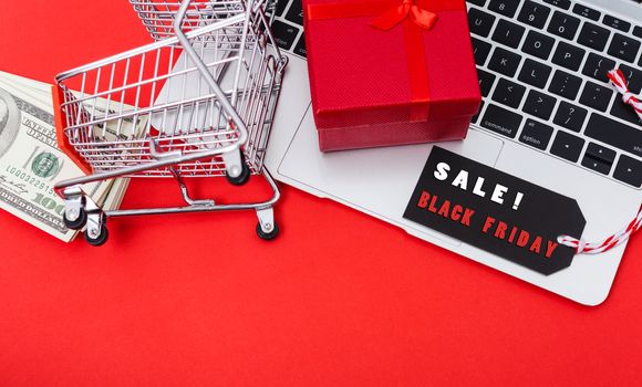 Online shopping, Promotion Black Friday Sale text on black tag with computer laptop and money on red background.