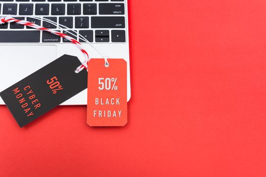 Online shopping Black Friday text with red tag and Cyber Monday text with black tag label on laptop computer, with copy space red background