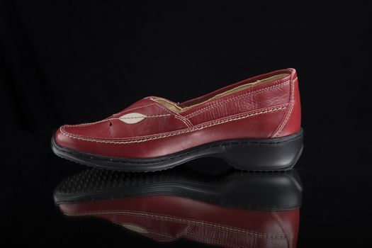 Female red leather shoe on black background, isolated product.