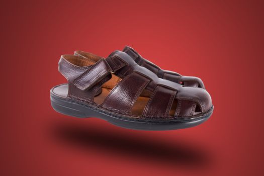 Pair of brown leather sandal on red background, isolated product.