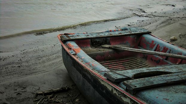 Small wooden boat destroyed  and worn by time and weather abandoned on the banks of a river in Italy.